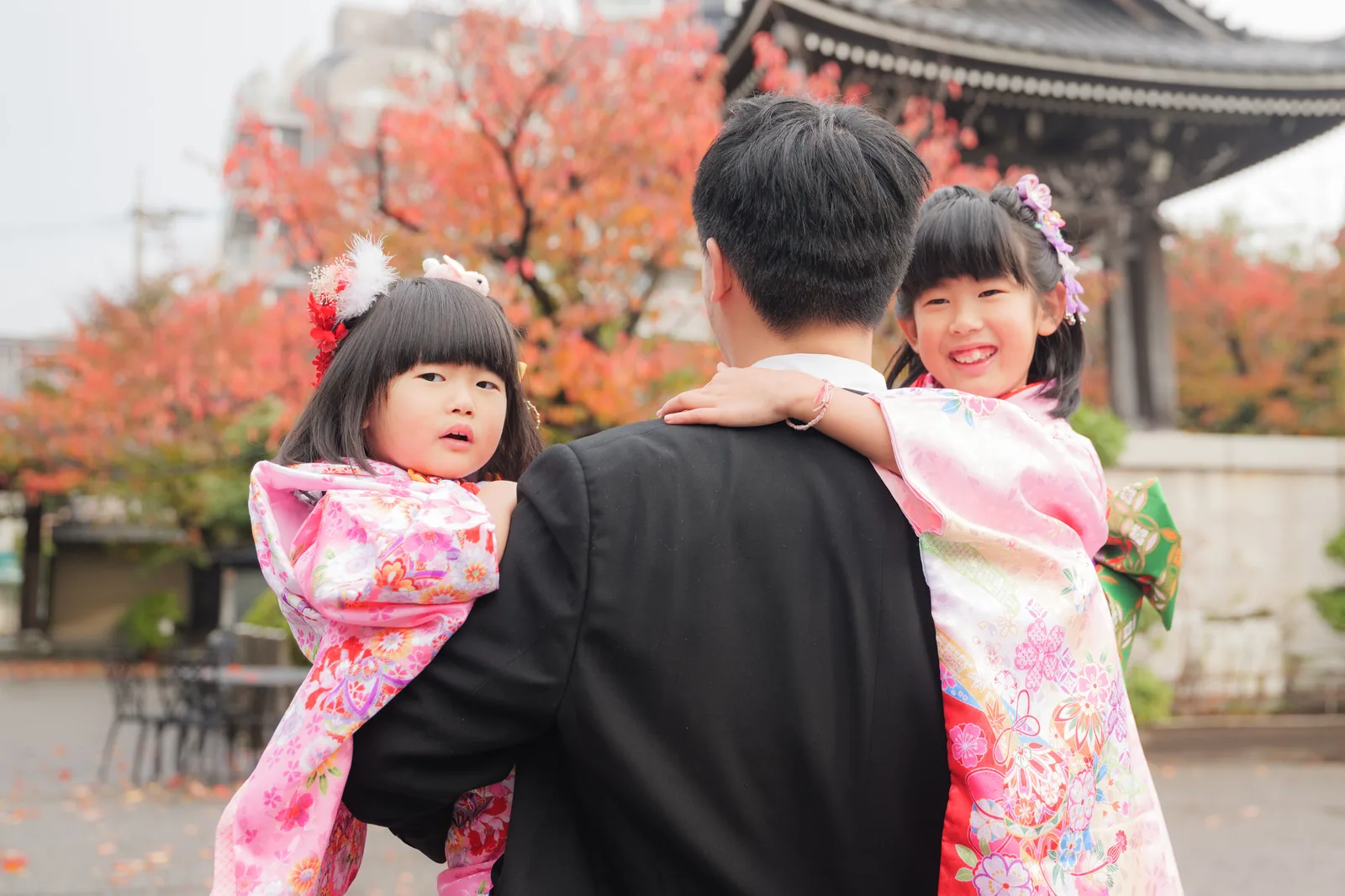 紅葉の境内でパパに抱っこされる着物姿の姉妹