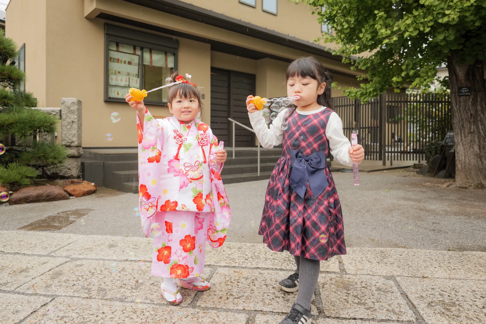 しゃぼん玉を吹いて遊ぶ被布姿の3歳の女の子とお姉ちゃん