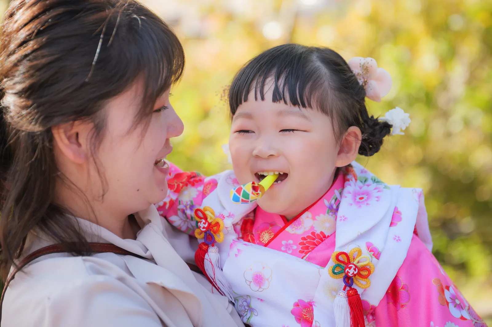 ママの腕の中で千歳飴を頬張る被布姿の3歳の女の子