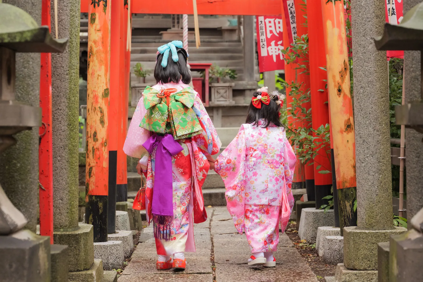 朱色の鳥居が続く参道を手をつないで歩く着物姿の姉妹