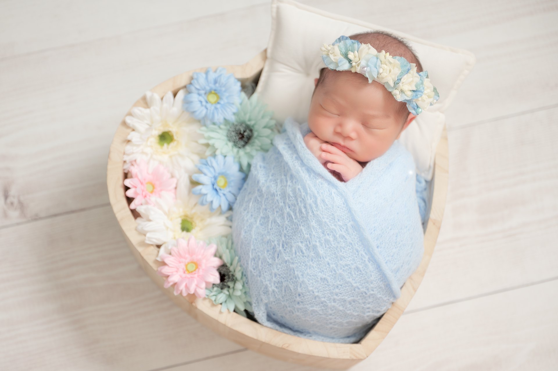 ハート型の器で青い花に囲まれて眠る赤ちゃんのニューボーンフォト